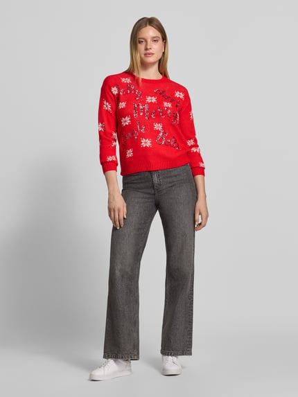 Frauenmodel trägt Pullover mit Pailletten-Schriftzug von VERO MODA, mehrfarbig, Strickoptik, Sternenmuster, Ganzkörperansicht von vorne