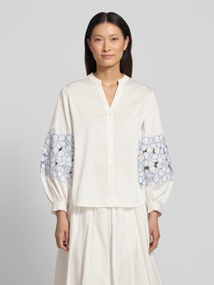 Modelka nosi Regular Fit Bluse mit Stitchings von HERZENS, biały bawełniano-elastanowy materiał, haft na rękawach, V-dekolt, przód z guzikami, Ganzkörperansicht von vorne.