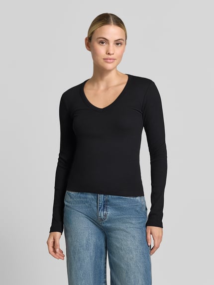 Frauenmodel trägt schwarzes Slim Fit Langarmshirt aus Baumwoll-Mix Modell 'CHLOE' von VERO MODA, kombiniert mit blauer Jeans, Ganzkörperansicht von vorne, Damen Langarmshirt von VERO MODA.