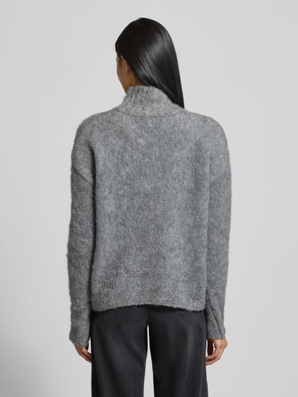 Frauenmodel trägt Strickpullover mit Stehkragen und überschnittenen Schultern von Milano Italy in Grau, melierte Textur, Ganzkörperansicht Rückansicht. Material-Mix mit Mohair-Anteil, Regular Fit, Rückenlänge 57 cm, Ärmellänge 76 cm.