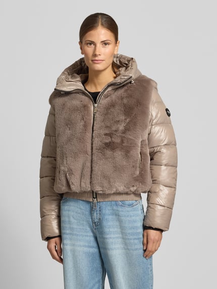 Frauenmodel trägt Steppjacke mit Kunstfell-Besatz Modell 'ONIKA' von khujo in Beige, glänzende Oberfläche, lockerer Schnitt, Nahaufnahme Oberkörper. Regular Fit, Kapuze mit Tunnelzug, Zweiwege-Reißverschluss, Rückenlänge 55 cm, Schulterbreite 44 cm, Brustweite 47 cm, Ärmellänge 65 cm.