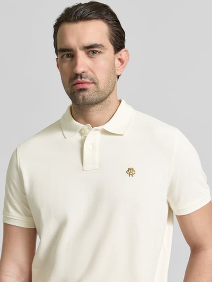 Męski model nosi Slim Fit Poloshirt mit Logo-Stitching von MCNEAL z czystej bawełny, krój slim fit, polokrag, kremowy, zbliżenie na górną część ciała.