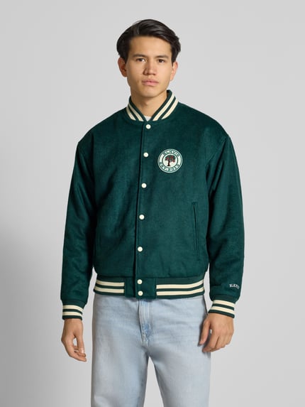 Männermodel trägt College Jacke mit Label-Patch von BLKVIS in Dunkelgrün, Material-Mix mit Woll-Anteil, Regular-Fit, Stehkragen, Knopfleiste, Eingrifftaschen, Ganzkörperansicht von vorne.