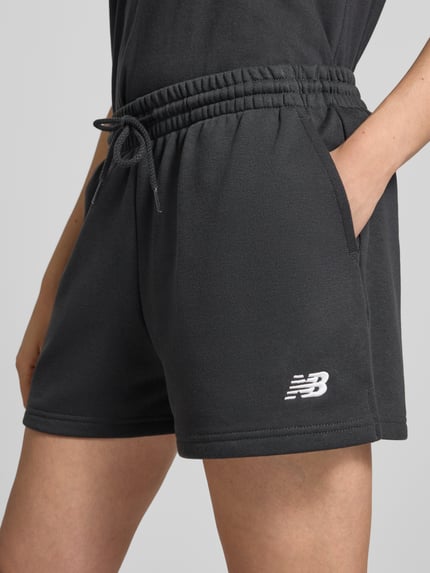 Frauenmodel trägt Sweatshorts mit Label-Stitching von New Balance aus Baumwoll-Mix, Regular-Fit, Elastischer Bund mit Kordelzug, Nahaufnahme Oberkörper.