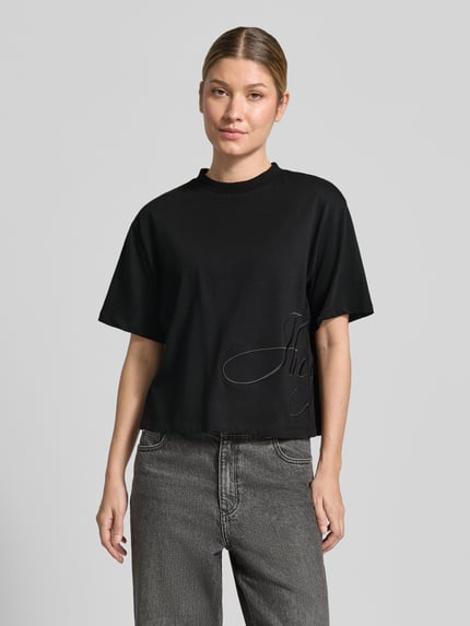 Kobiece modelka nosi czarny damski t-shirt z napisem, szare dżinsy, gładka struktura, model 'Duslant' od HUGO, zdjęcie całej sylwetki z przodu, damski t-shirt od HUGO