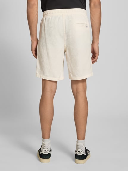Mężczyzna nosi Shorts mit Strukturmuster Modell 'JAIDEN' von Jack & Jones z bawełnianego materiału, jasny kolor, krój regular fit, strukturalna faktura, Szerokość w rozmiarze M: 41 cm, długość wewnętrzna nogawki: 21 cm, zdjęcie całej sylwetki z tyłu.