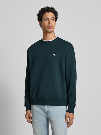 Męski model nosi Sweatshirt aus reiner Baumwolle od Calvin Klein Jeans, ciemnozielony kolor, prosty krój, ściągacze, widok całej sylwetki z przodu.
