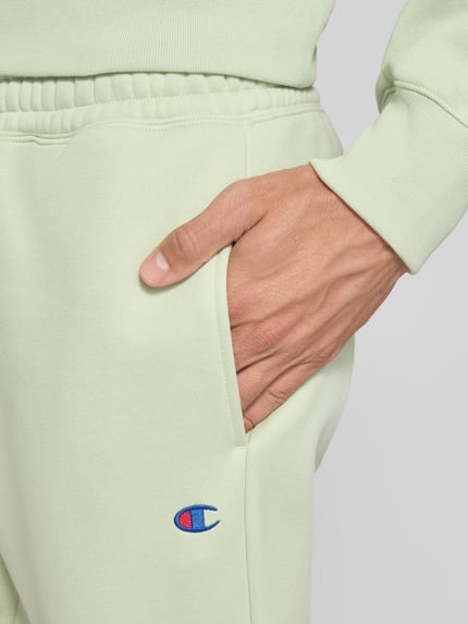 Männermodel trägt Sweatpants mit Label-Detail von Champion in Hellgrün, Baumwollmischung, Nahaufnahme Hüfte und Hand, Detailaufnahme.