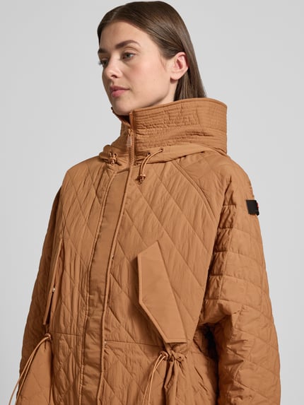 Frauenmodel trägt Relaxed Fit Jacke in Stepp-Optik Modell 'Texel' von Peuterey in Braun mit Stehkragen, Pattentaschen, Tunnelzug, Nahaufnahme Oberkörper. Rückenlänge 80 cm, Schulterbreite 50 cm, Brustweite 72 cm, Ärmellänge 59 cm.