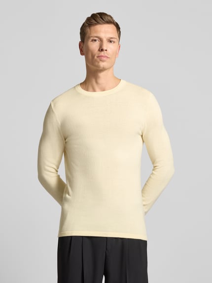 Männermodel trägt Strickpullover mit gerippten Abschlüssen Modell 'Irmino' von Drykorn in Creme, reine Baumwolle, Ganzkörperansicht von vorne.
