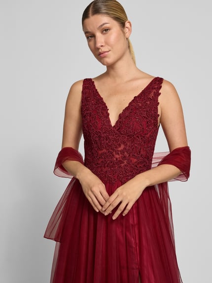 Vrouwenmodel draagt avondjurk met Spitze en strasssteinbesatz van Mascara in bordeauxrood chiffon, a-lijn, diepe v-hals, maxi-jurk, detailopname bovenlichaam. Context: Dames avondjurk van Mascara, chiffon, a-lijn, maxi-jurk, diepe v-hals, kant, met strass-steentjes, rugdecolleté, haakjes- en ritssluiting aan de achterkant, ruglengte bij maat 36: 155 cm, borstwijdte bij maat 36: 138 cm.