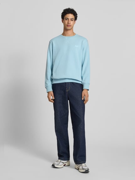 Männermodel trägt Sweatshirt mit Rundhalsausschnitt und Label-Stitching von Superdry in Hellblau, Baumwoll-Mix, Regular-Fit, Ganzkörperansicht von vorne.
