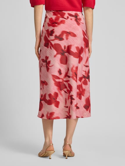 Vrouwenmodel draagt midirok met elastische band model 'YASPELLA' van YAS, roze-rode print, elastische materiaalmix, A-lijn, totale lengte maat S 83 cm, bandwijdte maat S 38 cm, geheelzicht achteraan.