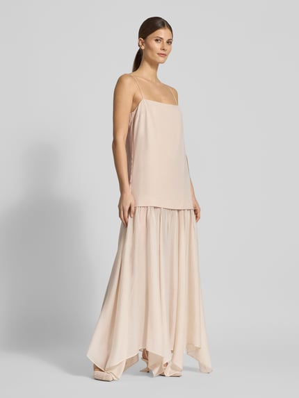 Modelka posiada na sobie dwuczęściową sukienkę na ramiączkach w długości maxi Zweiteiliges Trägerkleid in Maxilänge - curated by Vicky Heiler od SIC, jasny kolor, półprzezroczysta tkanina, fason straight, marszczenia, prosty dekolt, ramiączka spaghetti, długość tyłu w rozmiarze 38: 115 cm, szerokość w rozmiarze 38: 44 cm, widok całej sylwetki z przodu.