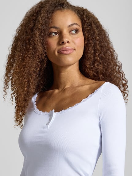 Frauenmodel trägt Longsleeve in Ripp-Optik mit Spitzenbesatz Modell 'MAYA' von NOISY MAY®, weiß, feine Knopfleiste, Nahaufnahme Oberkörper. Baumwoll-Elasthan-Mix, Slim Fit.