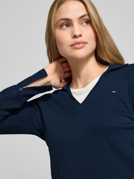 Vrouwenmodel draagt Slim Fit Langarmshirt aus reiner Baumwolle van Tommy Hilfiger, effen blauw, V-hals, logodetail, lange mouw, katoen, Nahaufnahme bovenlichaam.