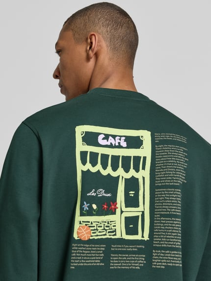 Männermodel trägt Sweatshirt mit Label-Details und Rundhalsausschnitt von Les Deux, Baumwoll-Elasthan-Mix, Regular-Fit, Rückenlänge 66 cm, Ärmellänge 70 cm, dunkelgrün mit Grafikprint, Nahaufnahme Oberkörper Rückansicht.