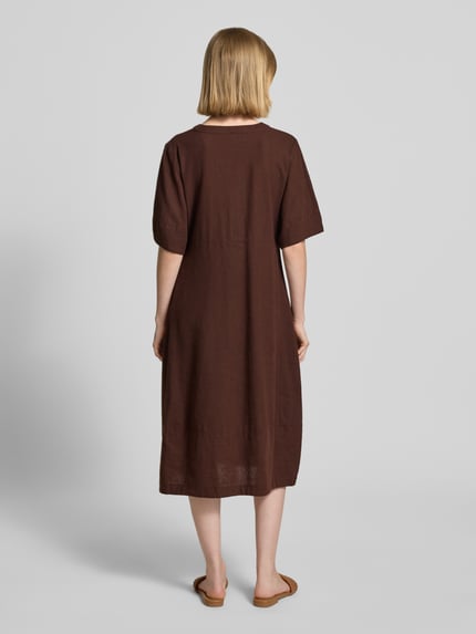 Frauenmodel trägt knielanges Kleid aus Leinen-Viskose-Mix Modell 'Lava' von FREE/QUENT in Braun, A-Linie, Ganzkörperansicht Rückansicht. Leicht strukturierte Textur, V-Ausschnitt, Knopfleiste, Rückenlänge 96 cm, Brustweite 43 cm, Ärmellänge 29 cm.