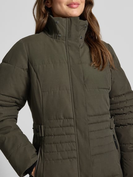 Frauenmodel trägt Jacke mit Kapuze und Label-Patch von G.I.G.A. DX in Olivgrün, Reißverschluss, strukturierte Oberfläche, Nahaufnahme Oberkörper. Material-Mix mit Baumwoll-Anteil, gerader Schnitt, seitliche Reißverschlusstaschen, gestrickte Ärmelabschlüsse.