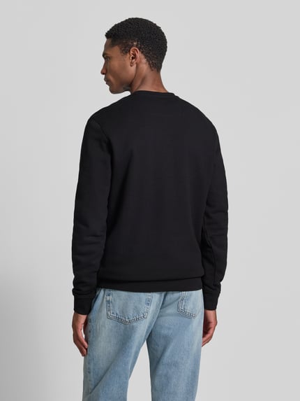 Männermodel trägt Regular Fit Sweatshirt mit Logo-Detail Modell 'Audley' von Guess, schwarzer Baumwoll-Mix, Rückansicht, Ganzkörperansicht Rückansicht. Herren Sweatshirt mit Rundhalsausschnitt und elastischen Abschlüssen, Rückenlänge 69 cm, Ärmellänge 69 cm bei Größe M.