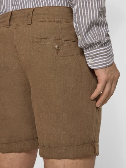 Männermodel trägt Leinenshorts mit Bindegürtel und Gesäßtaschen von MCNEAL in Braun mit Label-Stitching, Reine Leinen, Ganzkörperansicht Rückansicht.