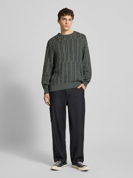Männermodel trägt Relaxed Fit Strickpullover aus Baumwoll-Mix Modell 'FILL RLX' von Only & Sons, unifarben, Zopfmuster, Ganzkörperansicht von vorne.