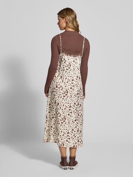 Frauenmodel trägt Relaxed Fit Midikleid mit Spitzenbesatz von OH APRIL, cremefarben mit braunem Muster, Midilänge, Ganzkörperansicht Rückansicht.