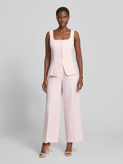 Frauenmodel trägt Bluse mit Viskose-Anteil Modell 'Haisley' von Forever New in zartem Rosa, tailliert, ärmellos, Ganzkörperansicht von vorne.