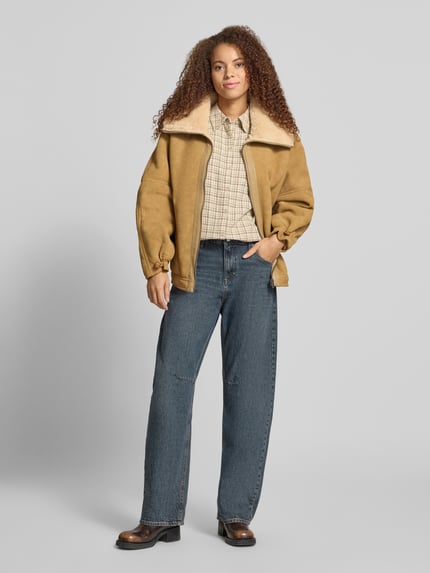 Frauenmodel trägt Kunstlederjacke mit Teddykragen von Esprit in Beige, kombiniert mit Jeans, strukturierte Oberfläche, Ganzkörperansicht von vorne, Rückenlänge bei Größe S 66 cm, Schulterbreite 58 cm, Brustweite 64 cm, Ärmellänge 54 cm.