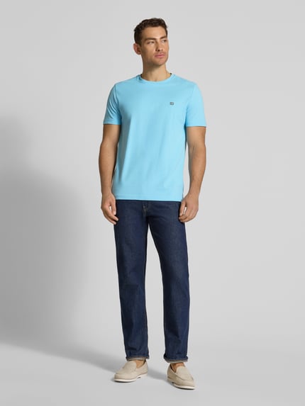 Męski model nosi T-Shirt aus Baumwolle mit Rundhalsausschnitt od Christian Berg Men, czysta bawełna, krój regular fit, okrągły dekolt, detal z logo, długość tyłu w rozmiarze M: 71 cm, kolor jasnoniebieski, proste cięcie, gładka tekstura, widok całej sylwetki z przodu.