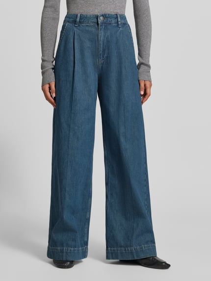 Frauenmodel trägt Wide Fit Jeans mit gelegten Falten von MYON, reine Baumwolle, mittelblauer Denim, Knopf- und Reißverschluss, Taschen, Nahaufnahme Unterkörper.