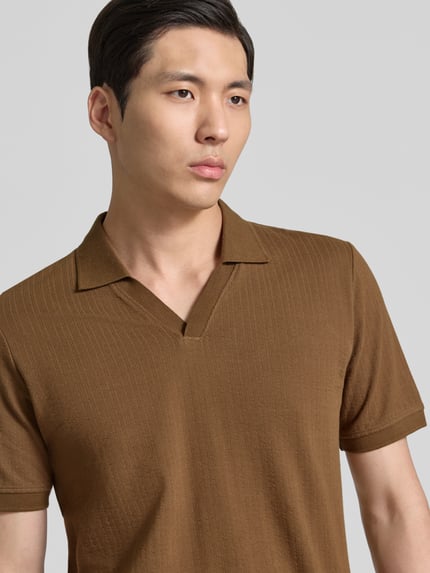Mannenmodel draagt Regular Fit Poloshirt aus reiner Baumwolle van s.Oliver RED LABEL in effen bruin, korte mouwen, jerseytextuur, label patch, polokraag, V-hals, detailopname bovenlichaam.
