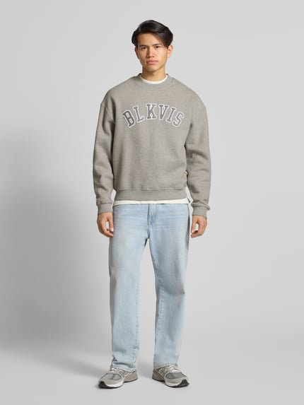 Männermodel trägt Sweatshirt mit Logo und Rundhalsausschnitt von BLKVIS, reine Baumwolle, relaxed Fit, graue Farbe, Ganzkörperansicht von vorne.