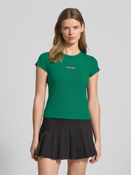 Kobiece modelka nosi T-shirt mit Rundhalsausschnitt und Label-Print von Calvin Klein Jeans, krój slim fit, mieszanka bawełny i elastanu, okrągły dekolt, nadruk z logo, długość tyłu w rozmiarze S: 42 cm, kolor zielony, widok całej sylwetki z przodu.
