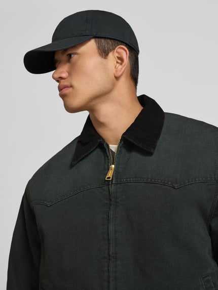 Männermodel trägt Jacke mit Reißverschluss und Label-Detail Modell 'Santa Fe' von Carhartt Work In Progress aus Baumwolle in Dunkelgrün, Nahaufnahme Oberkörper.