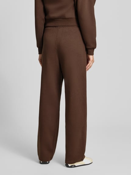 Vrouwenmodel draagt Wide Fit Sweatpants uit katoenmix Model 'Studio' van JJXX in bruin met logodetail en elastische band, binnenbeenlengte maat S 38 cm, full body achteraanzicht.