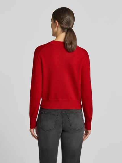 Frauenmodel trägt Strickpullover mit V-Ausschnitt Modell 'LIMONI' von MANGO in Rot, weiche Textur, elastische Abschlüsse, Ganzkörperansicht Rückansicht. Regular Fit, Rückenlänge 52 cm, Ärmellänge 58 cm.