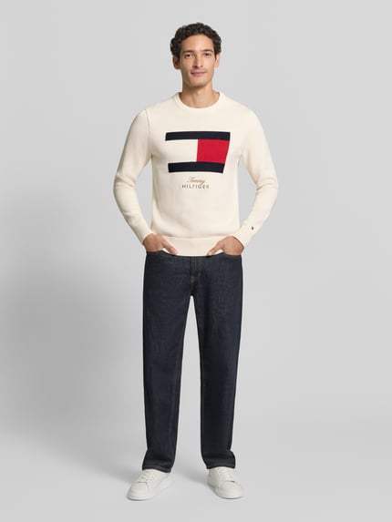 Männermodel trägt Regular Fit Pullover mit Motiv-Print von Tommy Hilfiger in Strickoptik mit Rundhalsausschnitt, Ganzkörperansicht von vorne.