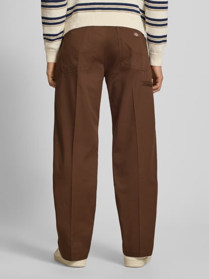 Männermodel trägt Loose Straight Fit Hose mit Bügelfalten von Dickies in Braun, Material-Mix mit Baumwoll-Anteil, Ganzkörperansicht Rückansicht.
