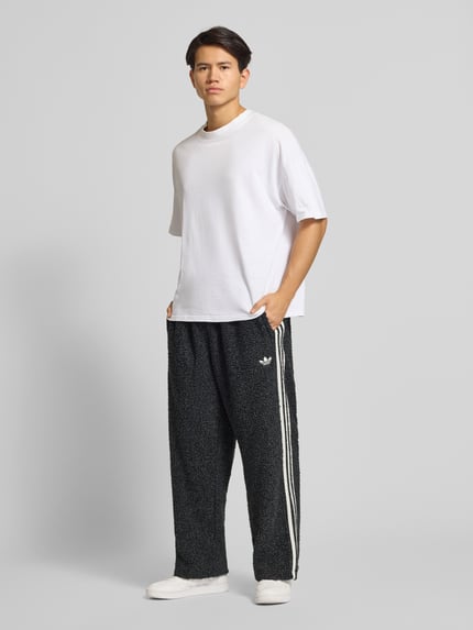Männermodel draagt Sweatpants met elastische tailleband van adidas Originals, bouclé-look, losse pasvorm, zwart met witte strepen, Ganzkörperansicht von vorne.