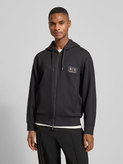Męski model nosi bluzę rozpinaną z mieszanki materiałów z modalu, krój regular fit, kaptur, naszywka z logo, zamek błyskawiczny dwustronny, wpuszczane kieszenie, Armani Exchange, długość tyłu 68 cm, długość rękawów 61 cm, kolor czarny, gładka faktura, widok z przodu, ujęcie całej sylwetki.