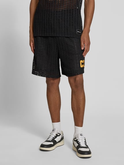 Männermodel trägt Straight Fit Shorts in Loch-Optik von COLUCCI, schwarz mit gelbem Logo-Stitching, elastischer Bund, Ganzkörperansicht von vorne.
