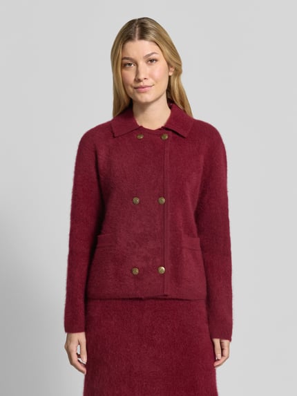Frauenmodel trägt Strickjacke aus reiner Wolle von Christian Berg Woman in Weinrot, doppelreihige Knopfleiste, Umlegekragen, taillierter Schnitt, seitliche Eingrifftaschen, weiche Struktur, Ganzkörperansicht von vorne.