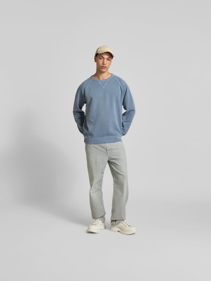 Männermodel trägt Relaxed Fit Sweatshirt aus Baumwolle von Closed in Blau mit Raglanärmel, Rundhalsausschnitt und elastischen Abschlüssen, Ganzkörperansicht von vorne.