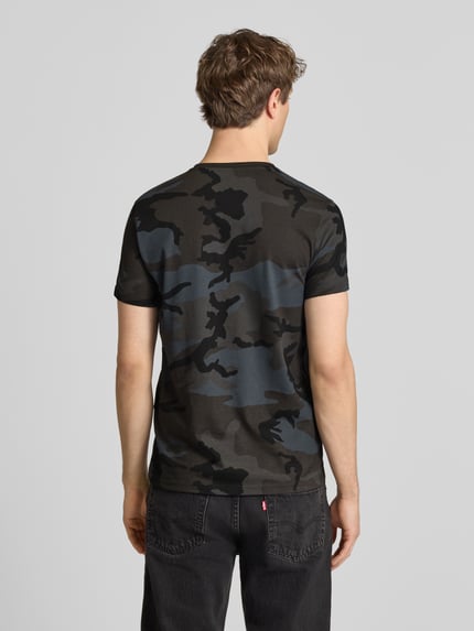 Männermodel trägt T-Shirt mit Label-Print von Alpha Industries in Grau-Schwarz Camouflage, Reine Baumwolle, Gerader-Schnitt, Rückenlänge 70 cm, Ganzkörperansicht Rückansicht.