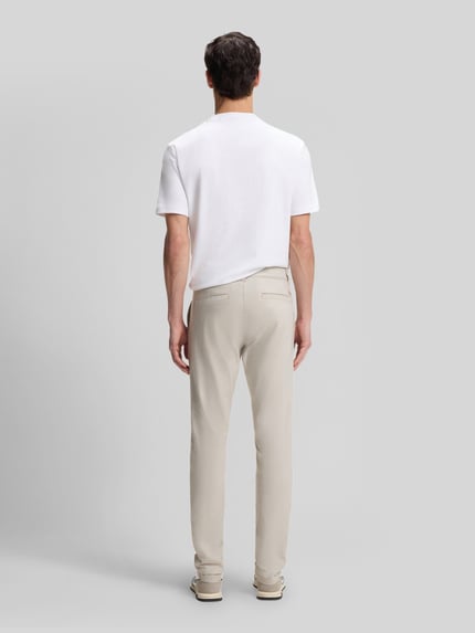 Männermodel trägt Slim Fit Chino aus Baumwoll-Mix mit Leinen und Viskose-Anteil von BOSS Orange in heller Denim-Optik, Ganzkörperansicht Rückansicht. Passform: Slim-Fit, Materialverarbeitung: Twill, Label-Patch, Label-Applikation, Mid Waist, Knopf und verdeckter Reißverschluss, seitliche Eingrifftaschen, Gesäßtaschen.