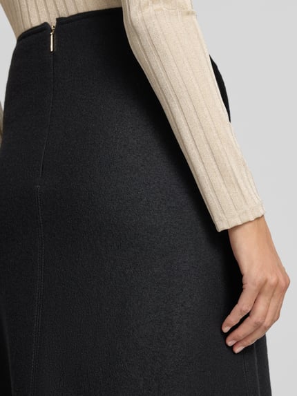 Frauenmodel trägt Midirock aus Schurwolle mit Reißverschluss von Marc Cain in Schwarz, A-Linie, Feinstrickstruktur, Detailaufnahme Rücken.