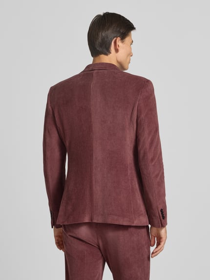 Männermodel trägt Slim Fit Sakko aus Baumwoll-Mix in Cord-Optik Modell 'Nick' von Zuitable, warmes Rotbraun, feine Rippen, Ganzkörperansicht Rückansicht.