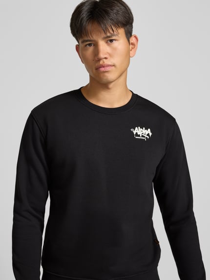Männermodel trägt Regular Fit Sweatshirt aus Baumwoll-Mix von Alpha Industries mit Logo-Print, Schwarz, Nahaufnahme Oberkörper.