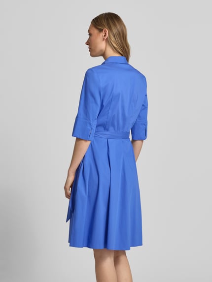 Modelka kobieca ma na sobie niebieską sukienkę koszulową do kolan 'Knielanges Hemdblusenkleid mit Bindegürtel' od Christian Berg Woman Selection, bawełniany materiał z domieszką stretchu, A-linia, zakryta listwa guzikowa, pasek, długość pleców w rozmiarze 36: 99 cm, szerokość w rozmiarze 36: 48 cm, długość rękawa w rozmiarze 36: 37 cm, widok całej sylwetki z tyłu.